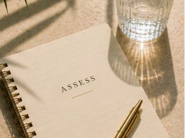 Notebook with "ASSESS" title, pen, and glass casting shadows.