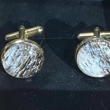 Round cufflinks with a textured silver design on a black background.