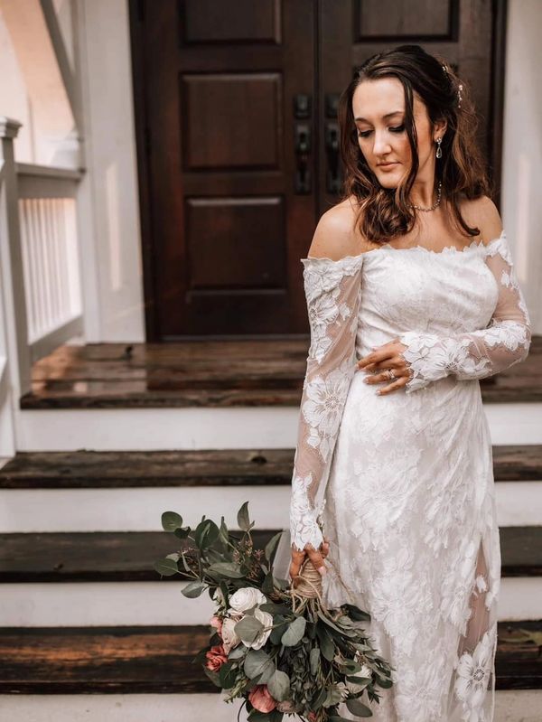Bride in lace dress holding bouquet on steps.