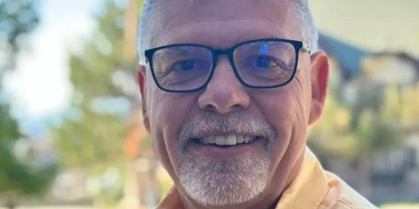Smiling man with glasses wearing a yellow Columbia shirt outdoors.