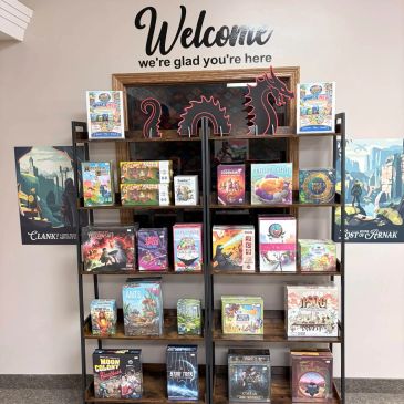 A shelf with various board games beneath a welcoming sign.