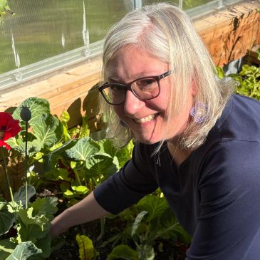 Woman gardening in a greenhouse, smiling warmly.