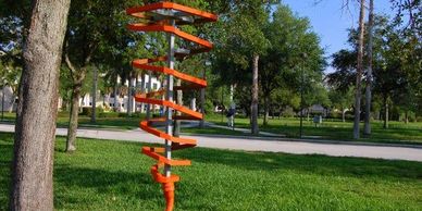 Orange spiral sculpture in a green park under blue sky.