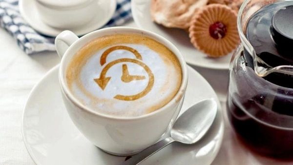 Cup of coffee with a clock and arrow design in the foam.