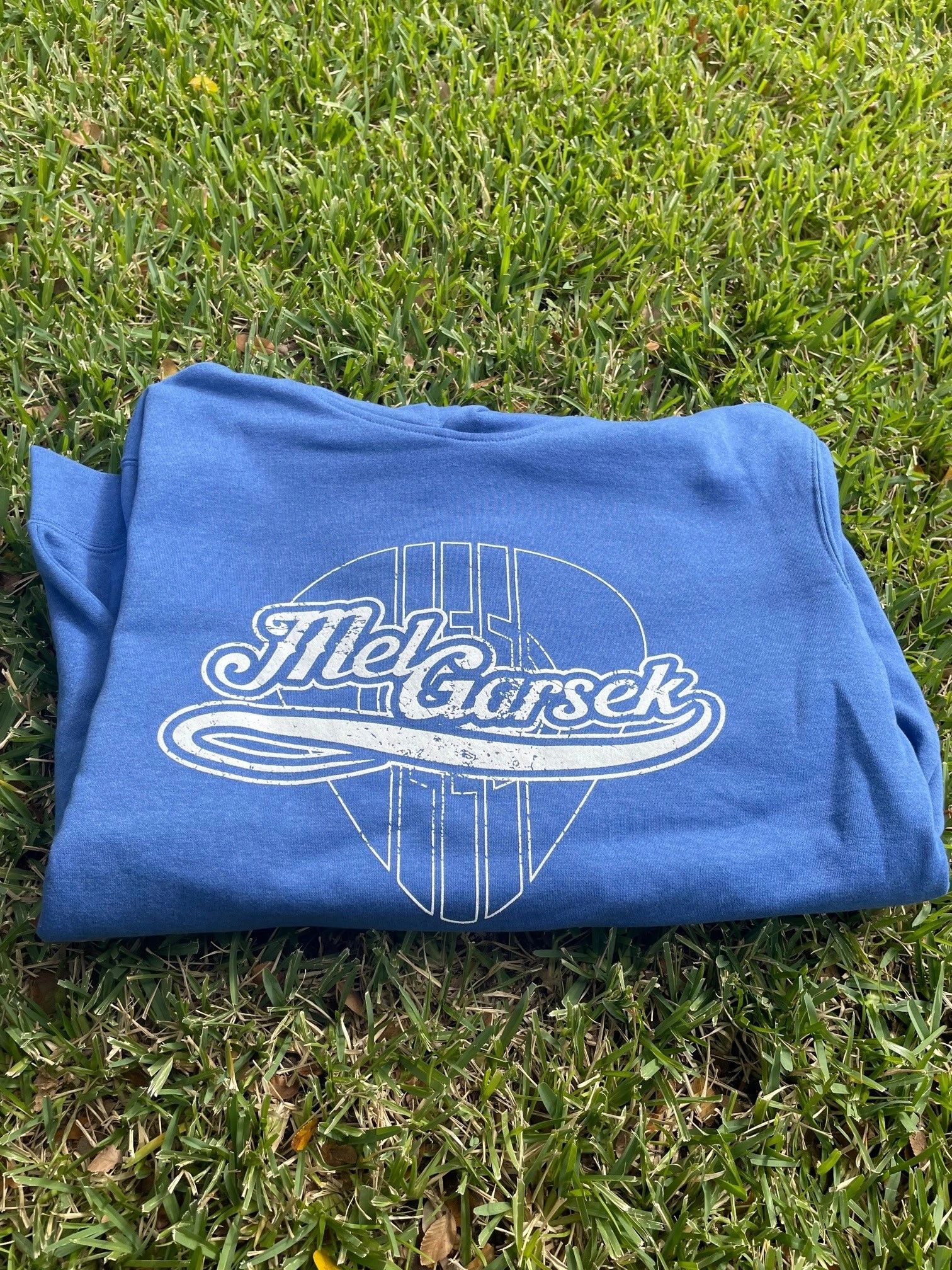 Blue Mel Garsek sweatshirt on green grass.