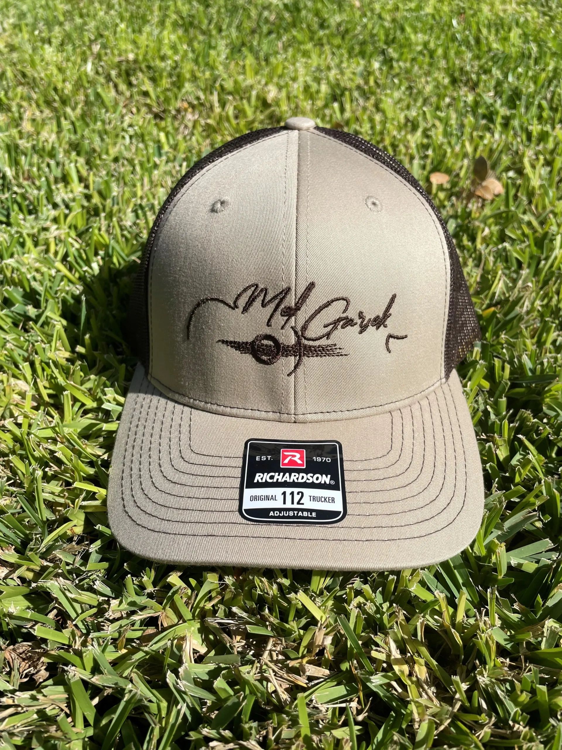 Tan and black trucker hat on grass with logo.