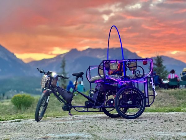Colorful rickshaw bike with LED lights at sunset in a mountainous area.