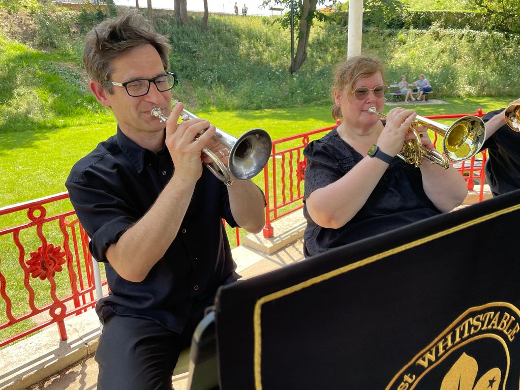 Two musicians playing trumpets outdoors in the sunlight.