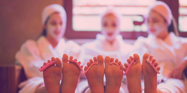 Three women relaxing with toe separators and facial masks in a spa.