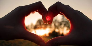 Hands forming a heart shape with the sun setting in the background.