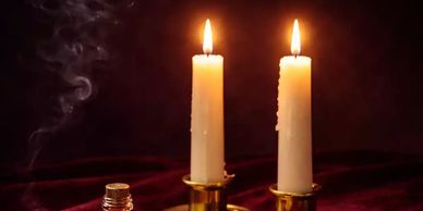 Two lit candles in brass holders with smoke rising from an unlit wick.