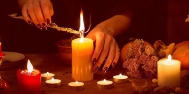 Hands lighting a large candle surrounded by smaller candles in a cozy setting.