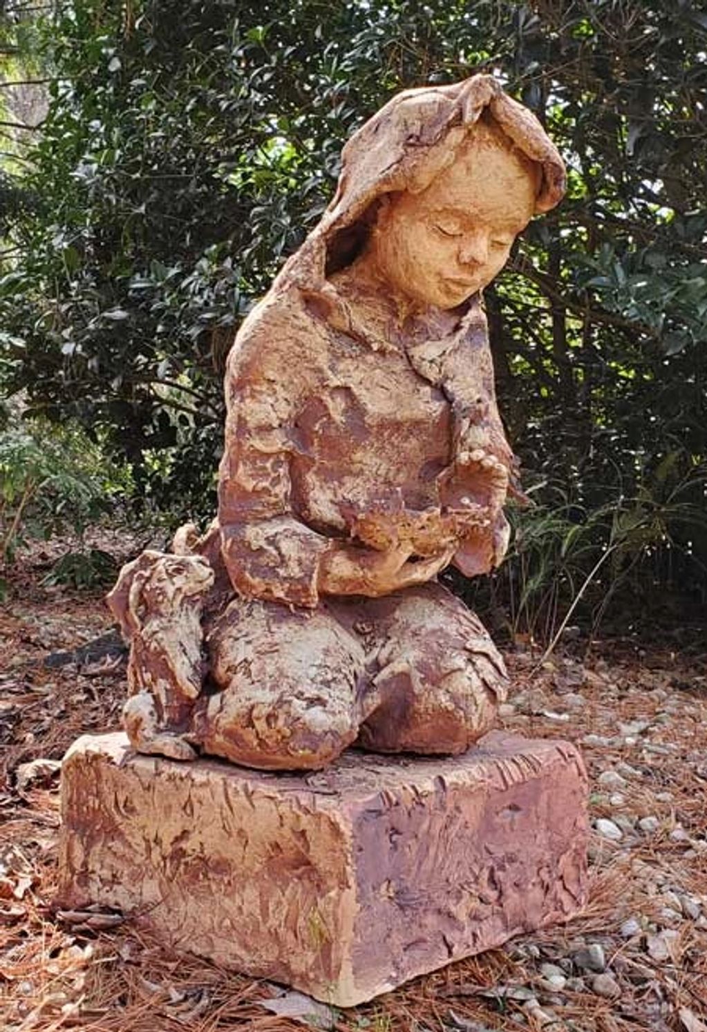 Rustic sculpture of a child with a dog in a natural setting.