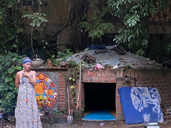 Woman standing near a rustic brick oven with plants around.