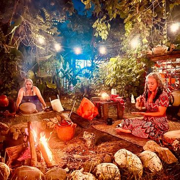 Two women engaged in a traditional outdoor ritual around a fire at night.