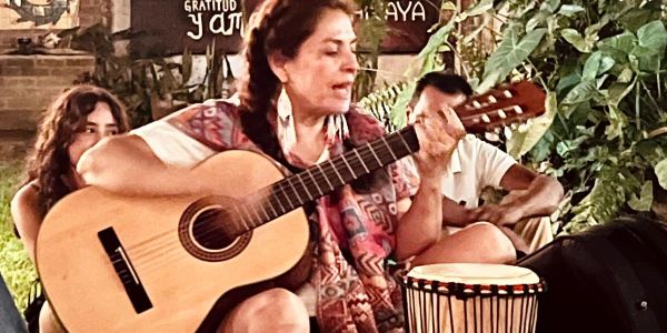 Woman passionately playing guitar surrounded by people outdoors.