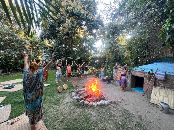 Group of people raising hands around a campfire in a lush garden.