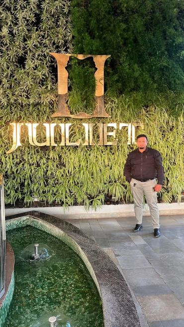 Man standing near a green wall with illuminated sign.
