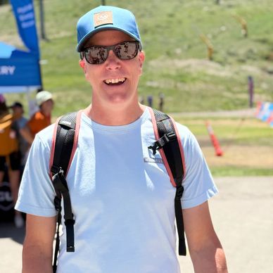 Man smiling outdoors wearing sunglasses and a blue cap.