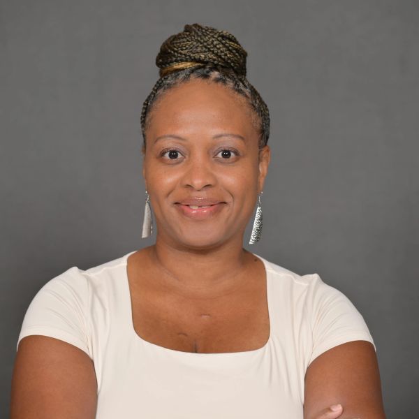 Confident woman with braided hair in a white top smiling against a gray background.