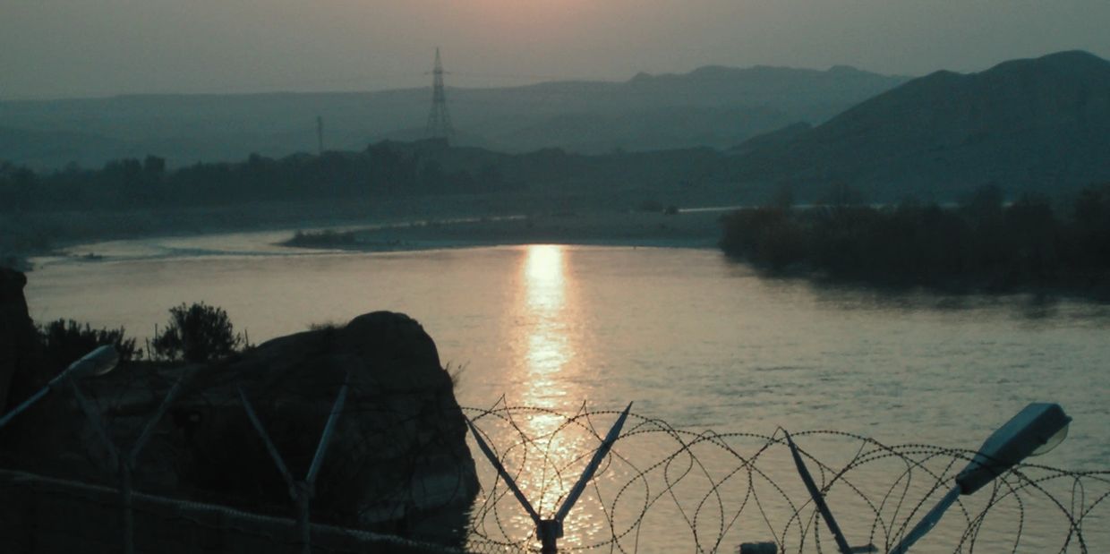 River at sunset with security fence, depicting high-risk or hostile environment