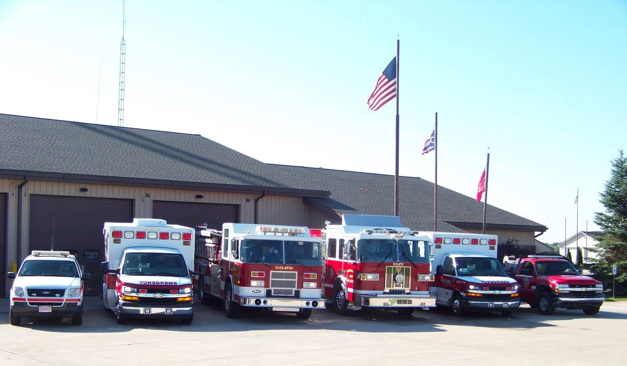 Fire station with emergency vehicles and flags at half-mast.