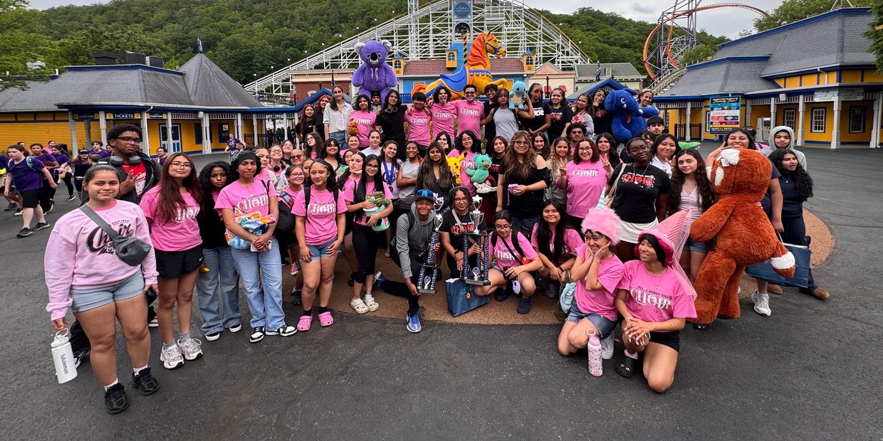 Large group of happy teenagers at an amusement park with trophies and stuffed animals.