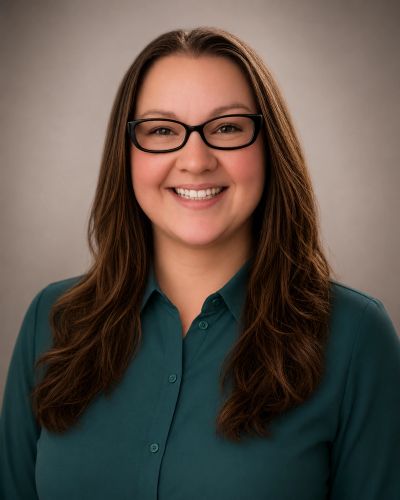 Smiling woman with long brown hair and black glasses wearing a teal blouse.
