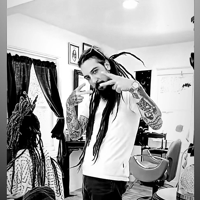 Tattooed man with long dreadlocks posing in a barbershop.