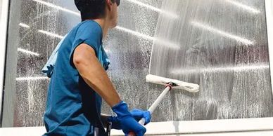 Worker cleaning a large glass window with a roller and wearing gloves.
