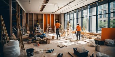 Workers renovating an interior space with ladders and tools scattered around.
