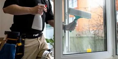 A person cleaning a window with a spray bottle and squeegee.