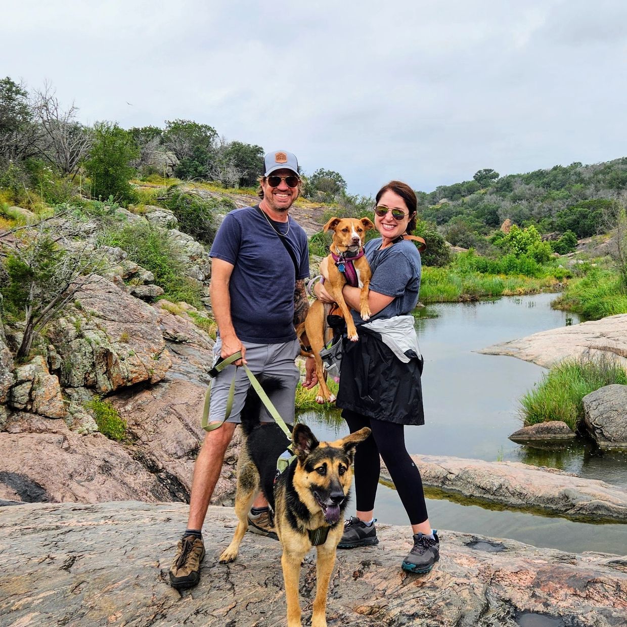 Couple hiking with two dogs near a rocky stream.