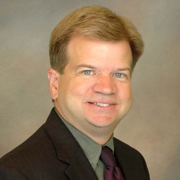Professional headshot of a man in a suit smiling.