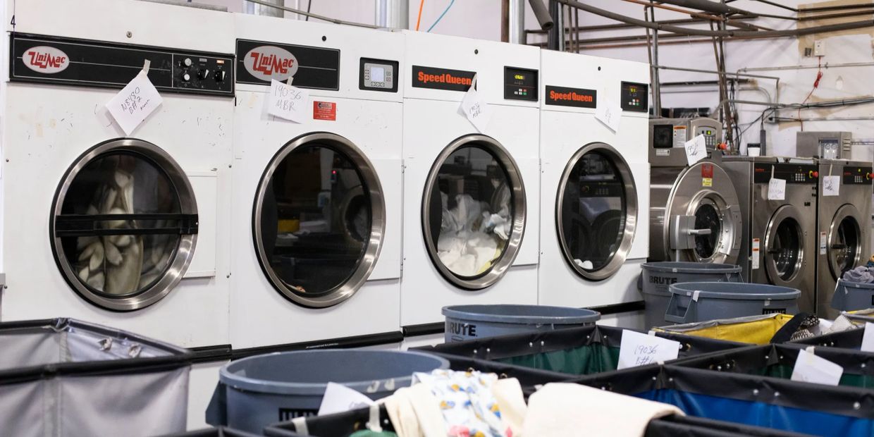 Industrial laundry machines lined up with laundry bins in front.
