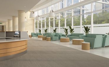 Modern office lobby with green chairs, wooden tables, and large windows.
