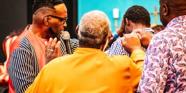 A man speaking into a microphone during a group prayer or blessing.