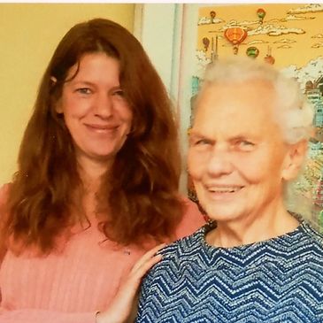 A smiling younger woman Frau Bieser and an elderly woman Frau Elwes posing together indoors.