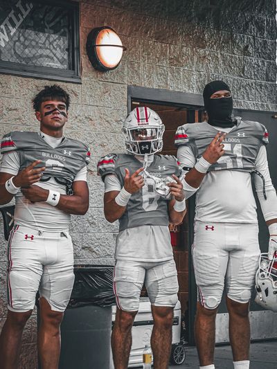 Three football players in grey Bulldogs uniforms posing for a photo.