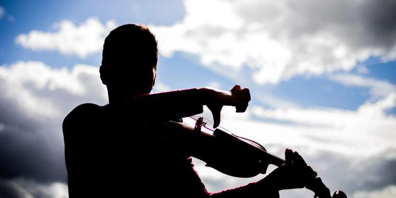 Silhouette of a person playing violin against a cloudy sky.