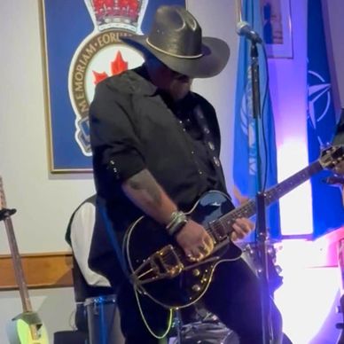 Man in cowboy hat playing electric guitar on stage.