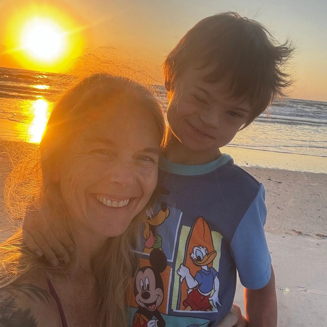 A woman and child smiling together on a beach at sunset.