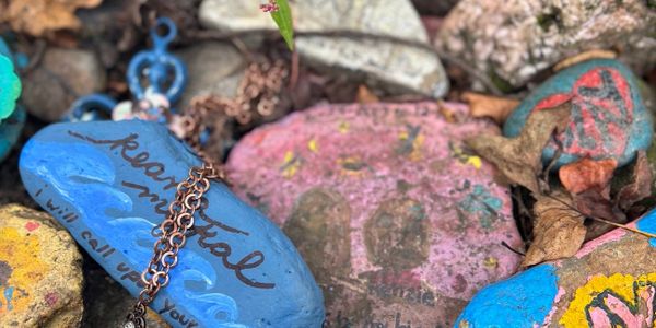 Colorful painted rocks with messages and a copper chain among leaves and stones.