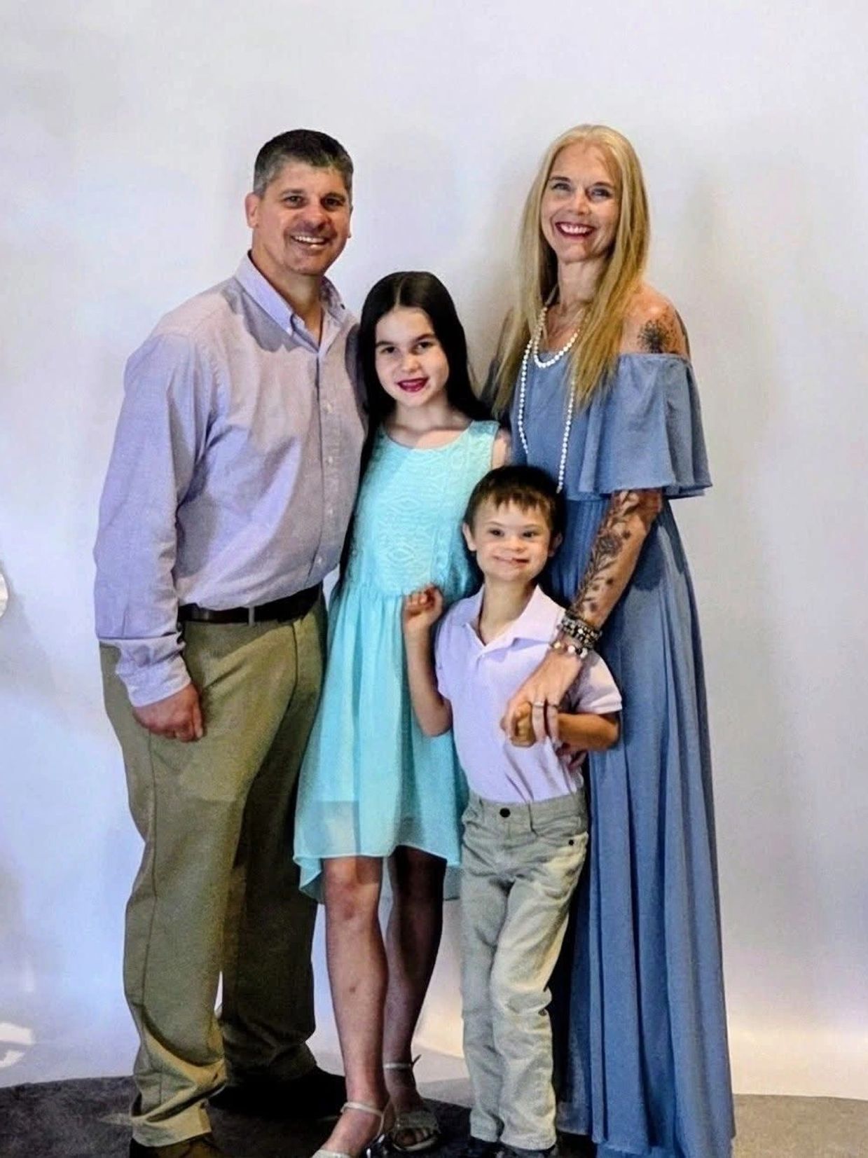 Smiling family of four posing together in coordinated outfits against a plain background.