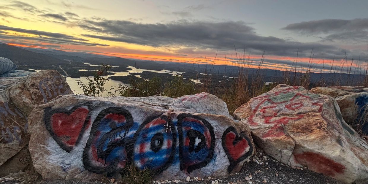 Sunset over a lake with rocks painted with hearts and the word 'GOD'.