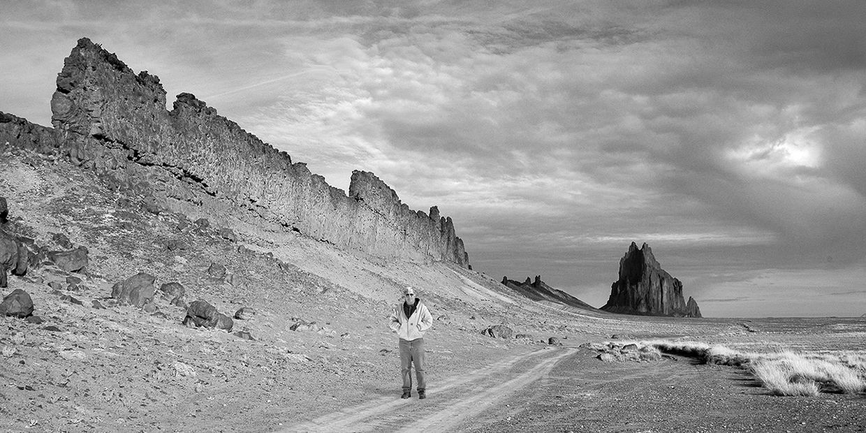 Person walking on a rocky path near cliffs under a cloudy sky.
