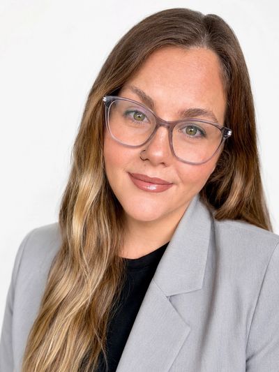 Smiling woman wearing glasses and a gray blazer.