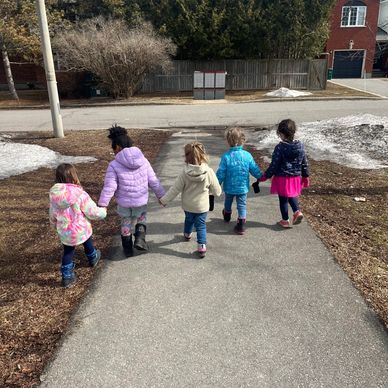 5 girls holding hands and walking in a line. Picture is of their backs