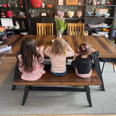 3 children eating their lunch. Taken of their backs at a beautiful large wooden dining table.