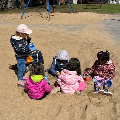 5 children sitting in a sandbox at the park